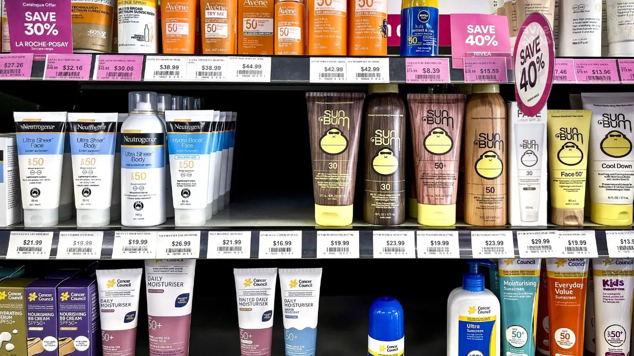 Store shelves stocked with sunscreen bottles and tubes, with price tags and sale signs.