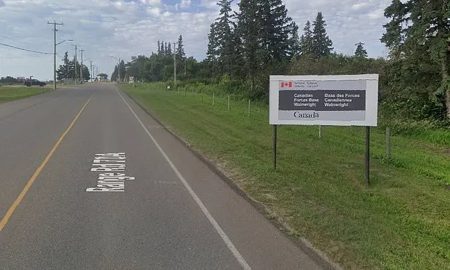 Rural road beside a sign reading Canadian Forces Base Wainwright, Canada, with trees.