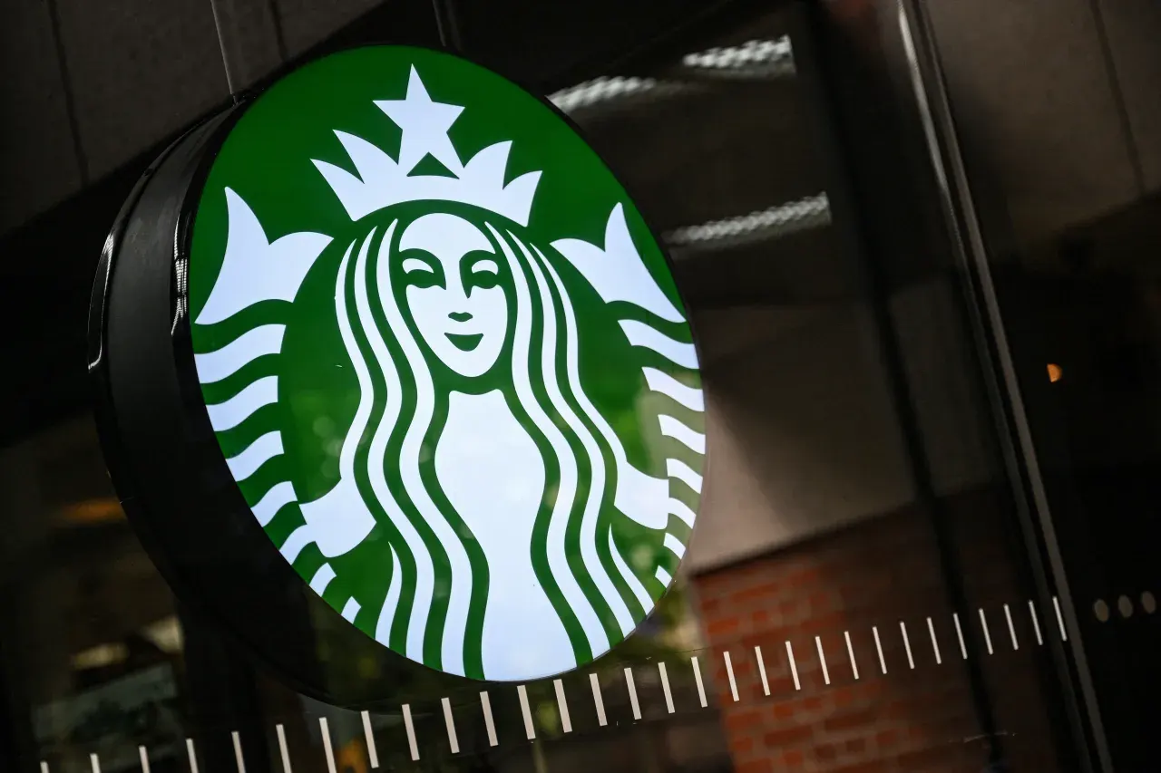 Illuminated green and white Starbucks logo sign mounted on a store exterior wall.