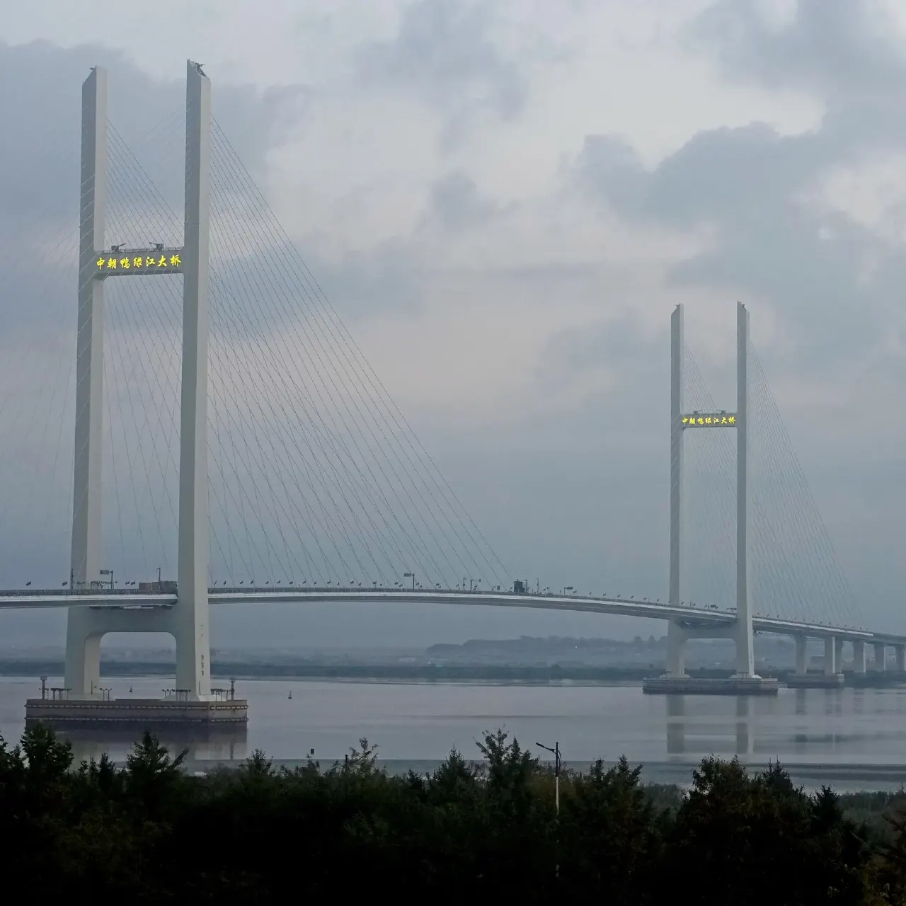 Cable-stayed bridge over river with twin white pylons and illuminated Chinese-character signage.