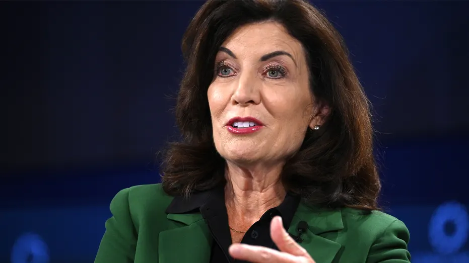 Woman in green blazer gesturing while speaking against a dark blue backdrop.