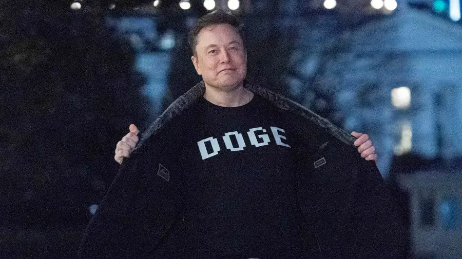 Man in dark jacket holding lapels open, wearing black DOGE sweatshirt at dusk