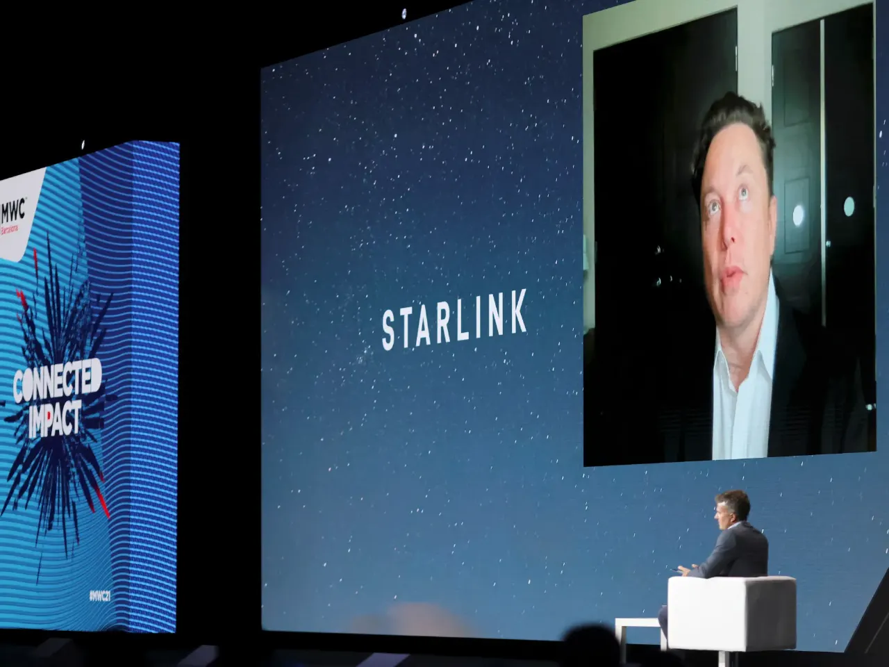 Conference stage: a man on a large screen beside a Starlink wordmark slide, with a seated presenter.