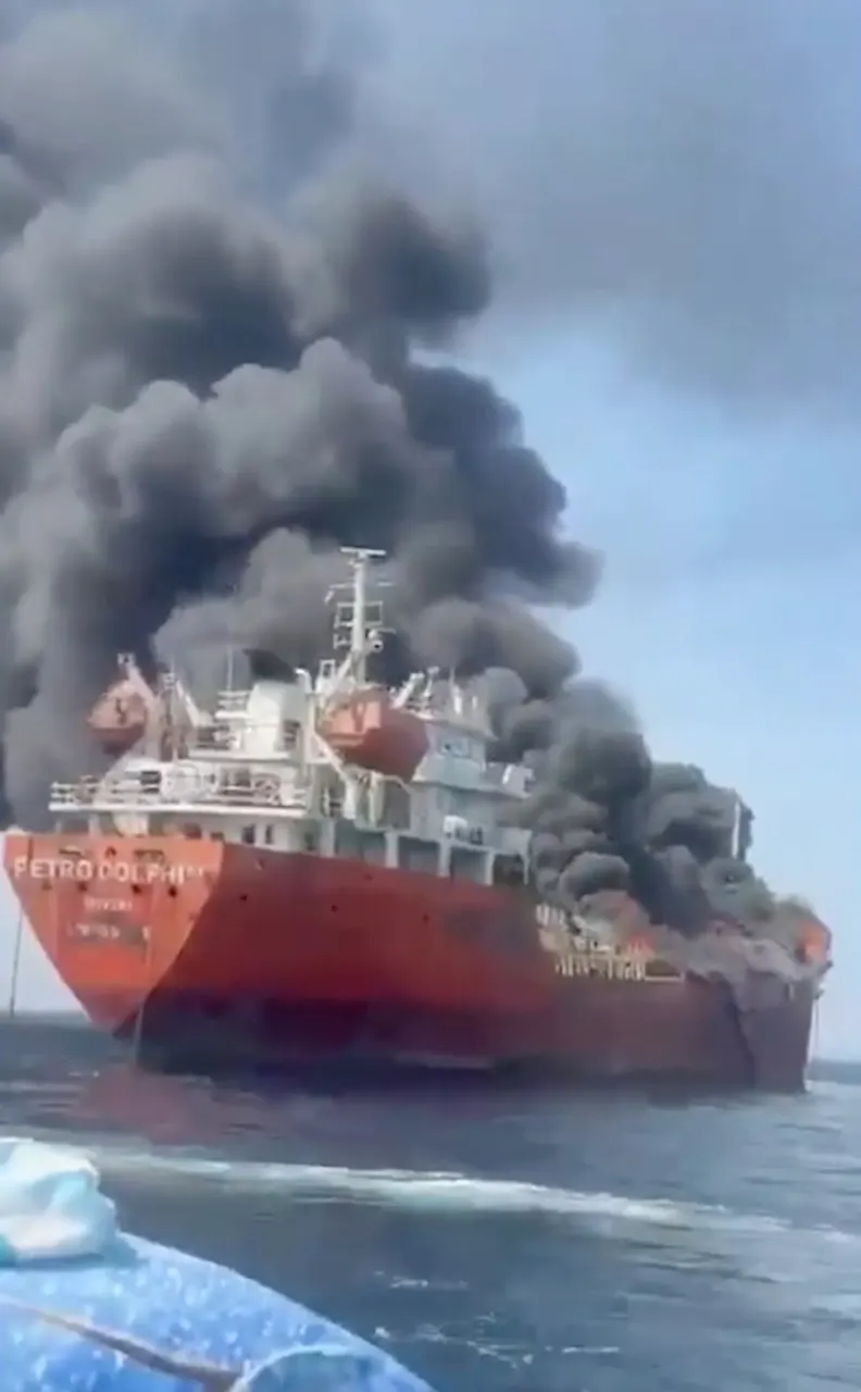 Red tanker ship Petro Dolphin billowing thick black smoke at sea, taken from a nearby boat.