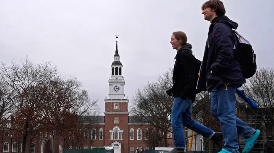 Two students walk past Dartmouth's brick Baker Library tower on a cloudy day.