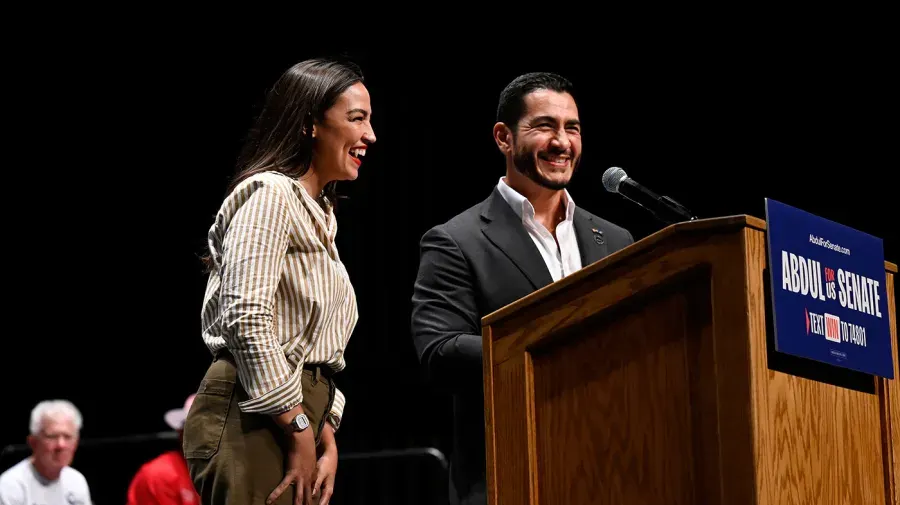 Two smiling people at a wooden podium with a campaign sign reading Abdul for US Senate.