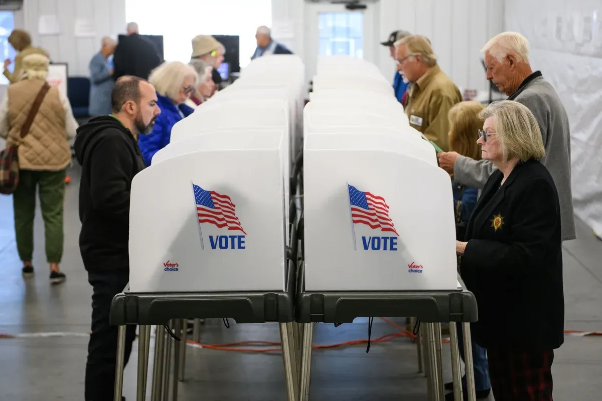 Voters using white VOTE privacy booths at a polling place, with an American flag on each booth.
