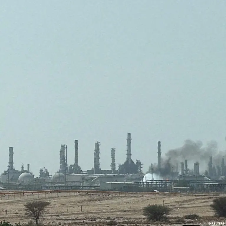 Industrial refinery with smokestacks and storage tanks, smoke rising, under hazy sky.