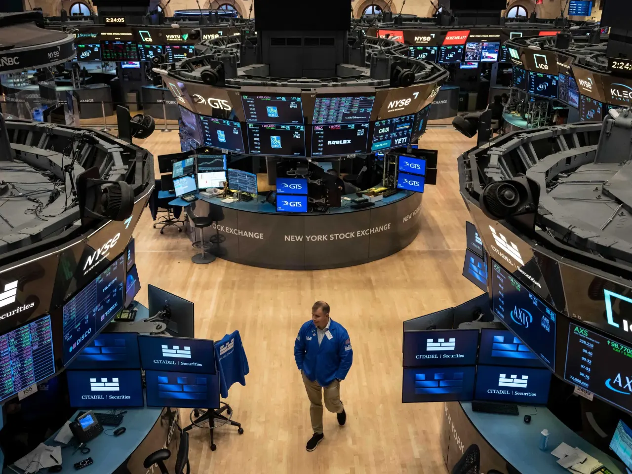 Wide view of New York Stock Exchange trading floor with screens and a lone trader walking