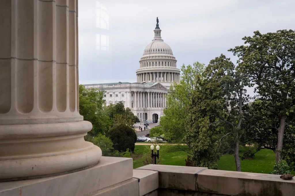 The U.S. Capitol dome viewed through a stone column and trees on a cloudy day