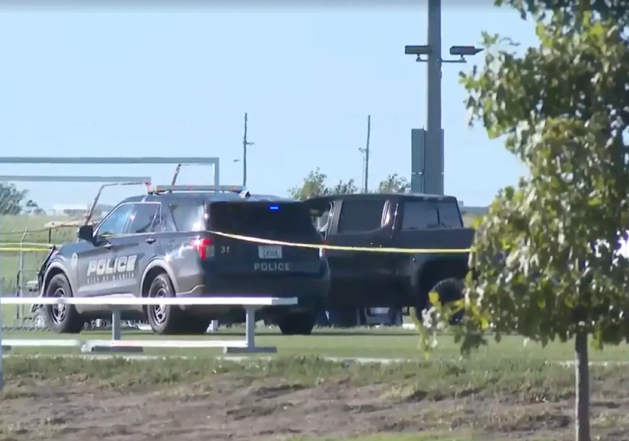 Police SUV and a dark pickup behind yellow tape on a grassy field