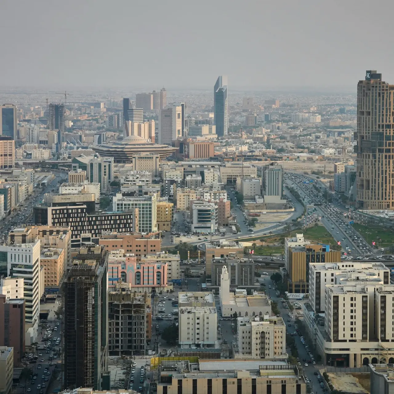 Aerial view of a hazy city skyline with high-rise towers and busy traffic roads.