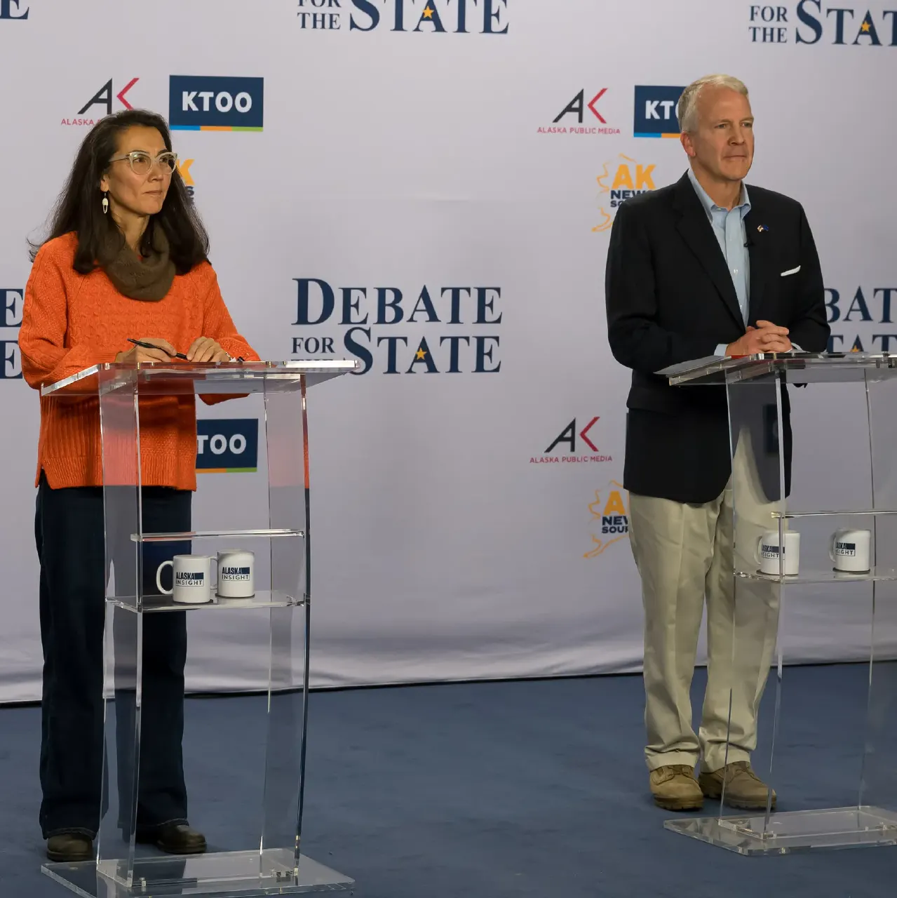 Two debate candidates stand at lecterns before a Debate for the State backdrop with station logos.