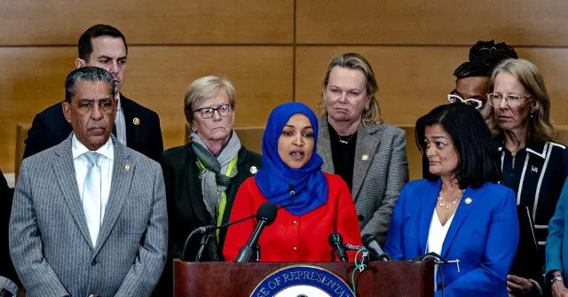 Group of congresswomen and congressmen at a press lectern bearing the House of Representatives seal.