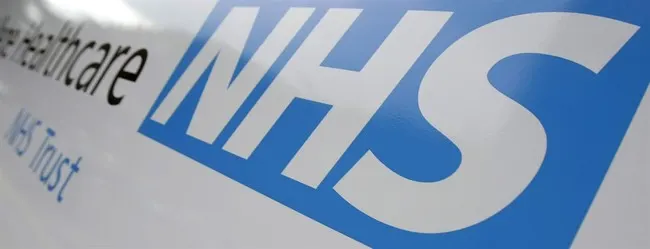 Close-up of the NHS logo in blue and white on a sign reading NHS Trust