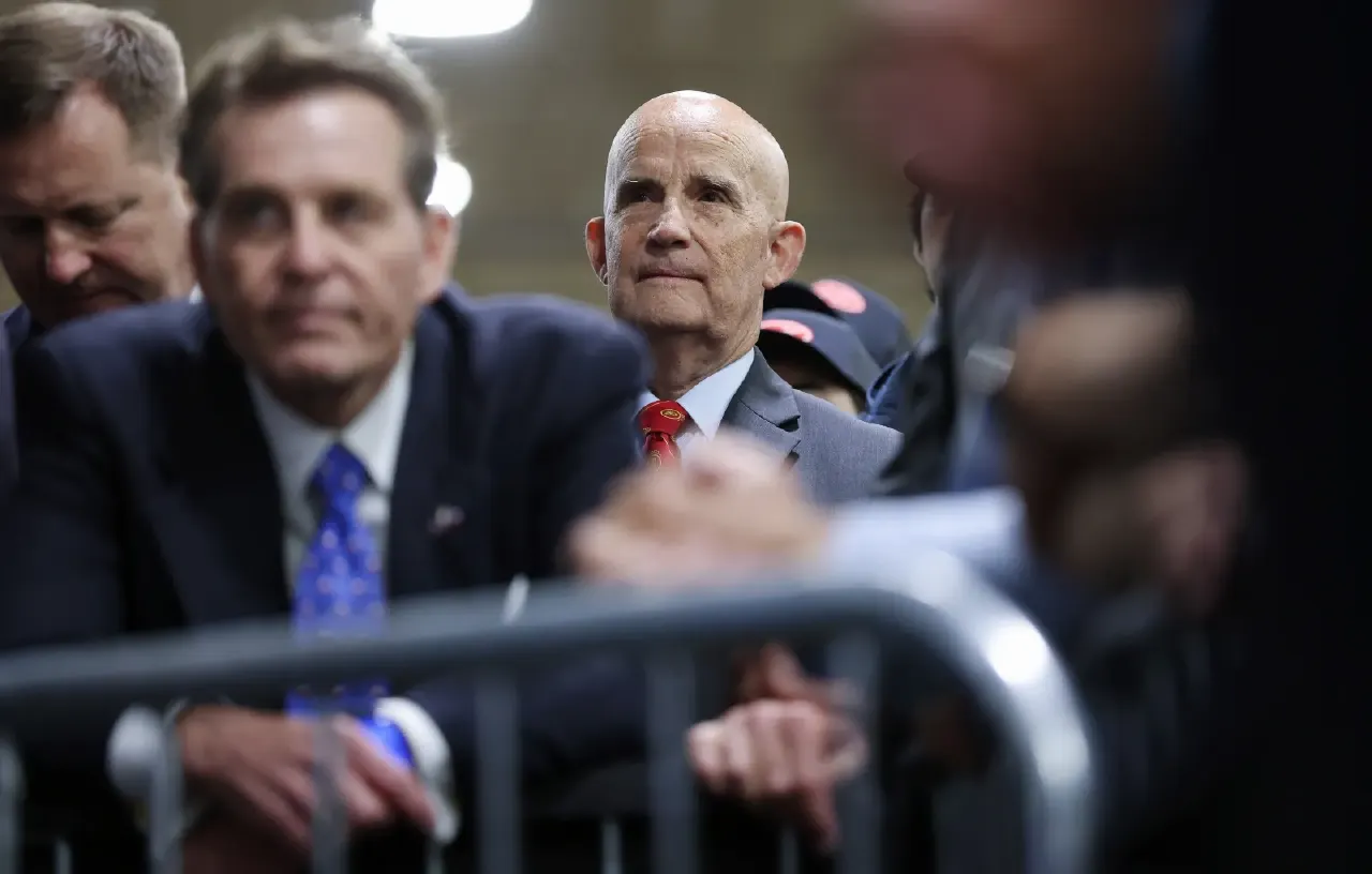 Older men in suits behind a metal barricade, watching an event, with blurred foreground figures.