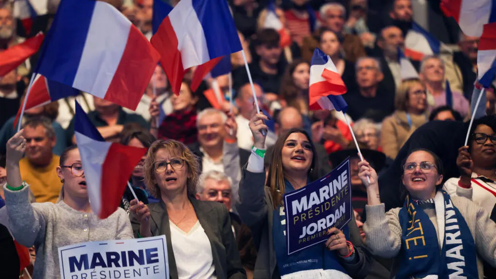 Cheering rally crowd waving French flags and holding Marine Présidente campaign signs.