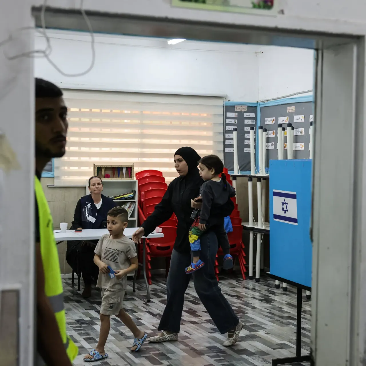 Woman with child and boy walk past a voting booth bearing an Israeli flag at a polling station.