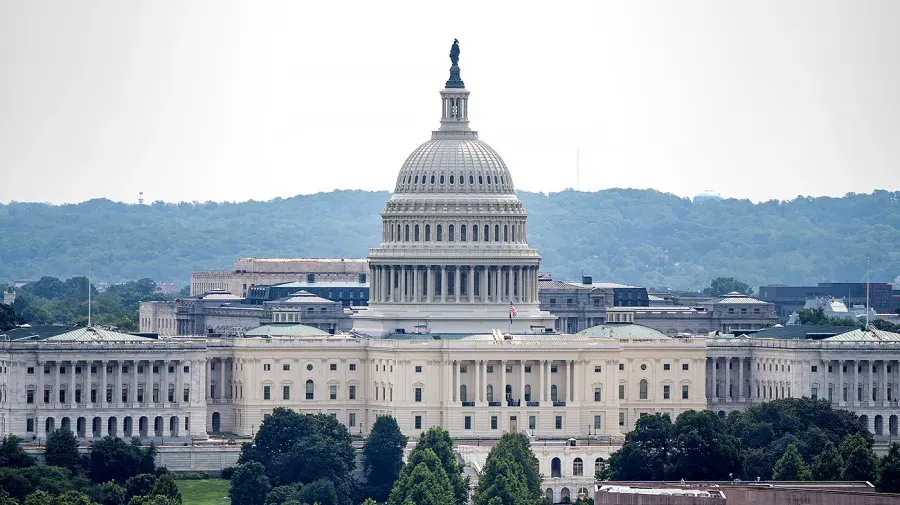 The U.S. Capitol dome and building viewed from a distance over trees on a hazy day.