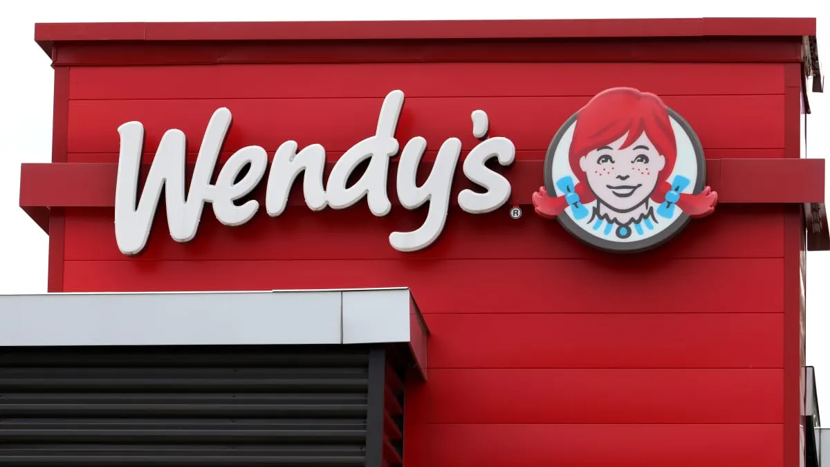 Wendy's restaurant sign with script logo and red-haired girl emblem on red building facade