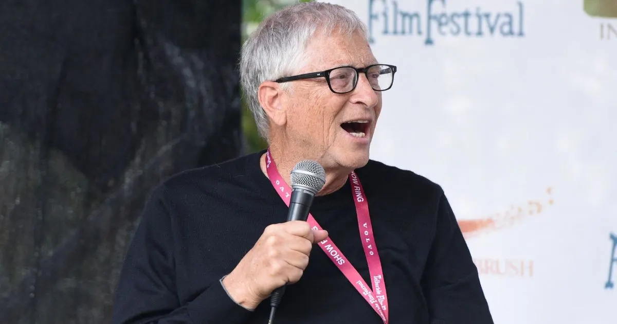 Older man with glasses speaks into a microphone at a film festival event backdrop.