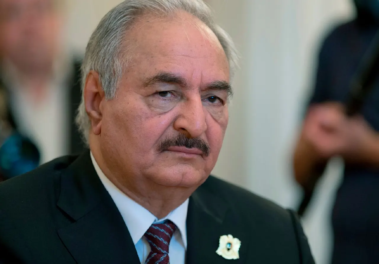 Older man with grey hair and moustache in dark suit, lapel pin, serious expression.