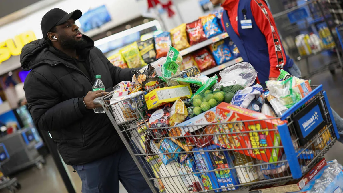 Shopper pushes a Walmart cart filled with snacks and groceries in a store aisle.