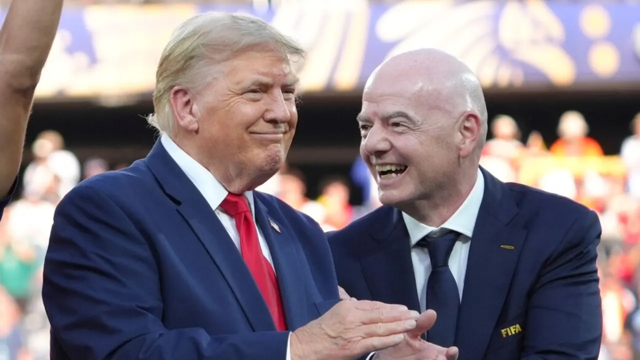 Two men in dark suits smiling at a stadium event, one wearing a visible FIFA pin.