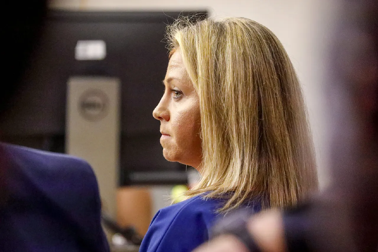 Woman in blue jacket in profile, looking off to the side in a courtroom setting.