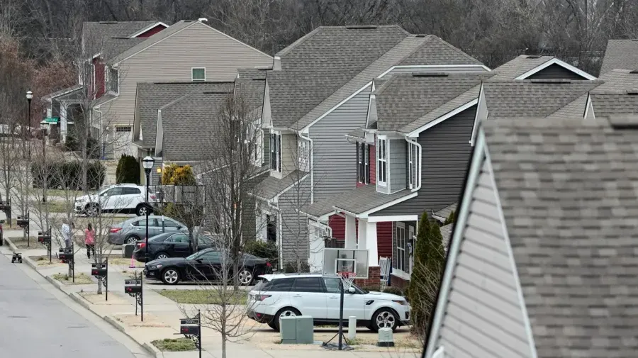 Rows of suburban houses with shingle roofs and parked cars on a residential street.