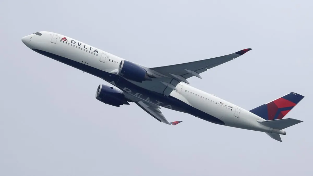 Delta Air Lines airliner with Delta logo climbing against a plain grey sky.