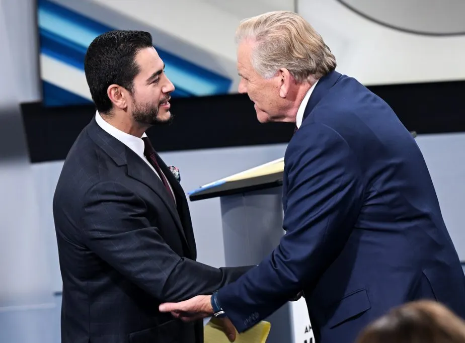 Two men in dark suits shaking hands on a debate stage set