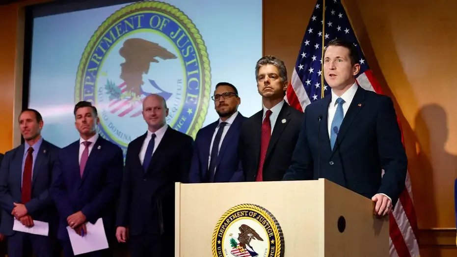 Men in suits at press podium before Department of Justice seal and American flag