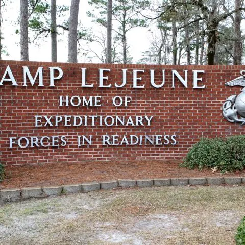 Brick entrance sign reading Camp Lejeune, Home of Expeditionary Forces in Readiness, with Marine emblem.